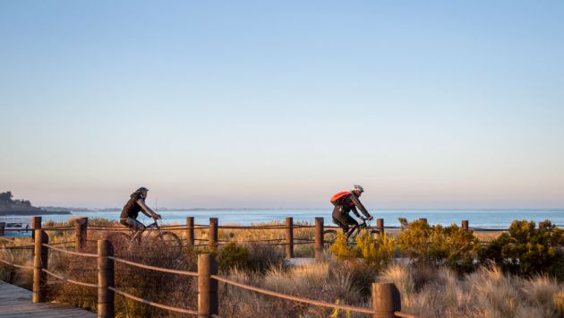 Two people cycling along the bay at sunset